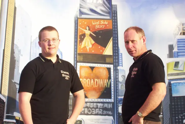 Darren and Colin in black Black Box Boys polo shirts in front of a big Broadway themed backdrop