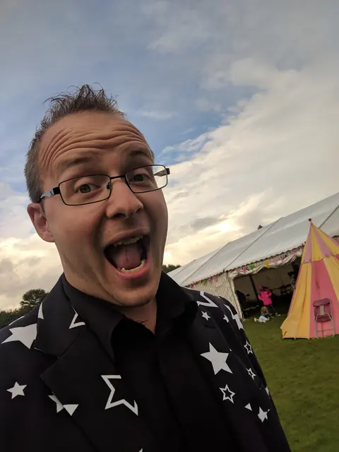 Darren pulling a big surprised face at an outdoor event in a star print shirt
