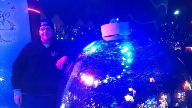 A Black Box Boy standing next to a giant glowing Christmas bauble under blue lights