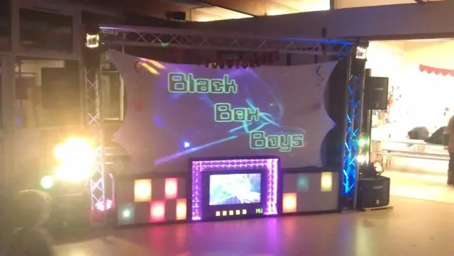 A Black Box Boys stage with a lit backdrop, glowing panels and a screen built into the DJ booth