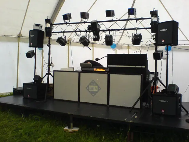 A stage in a marquee with a lighting truss, speakers and the DJ booth